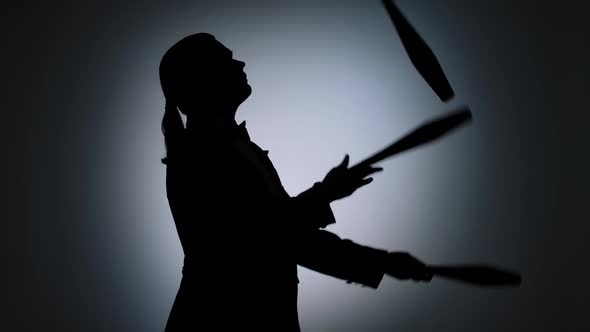 Side View Black Silhouette of Man Juggling with Pins in the Spotlight