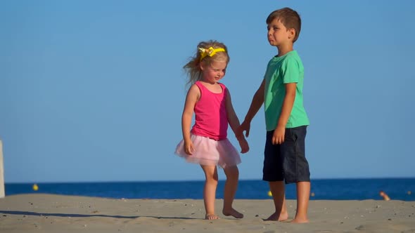 Little Boy and Girl in the Pink Skirt are Playing on the Beach