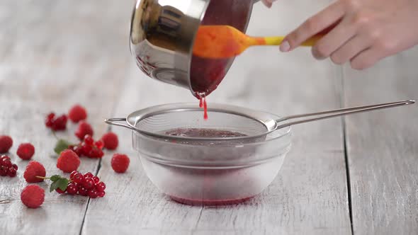 Chef Pushes Red Berry Fruit Through Kitchen Sieve in Glass Bowl.