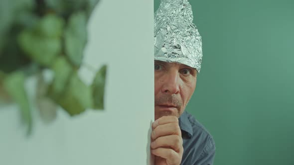 A Frightened Man in a Protective Foil Cap Peeking Strangely Around the Corner