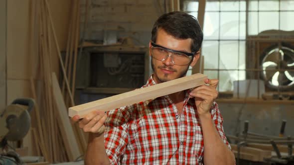 Bearded Carpenter Examining Wood Piece After Grinding It