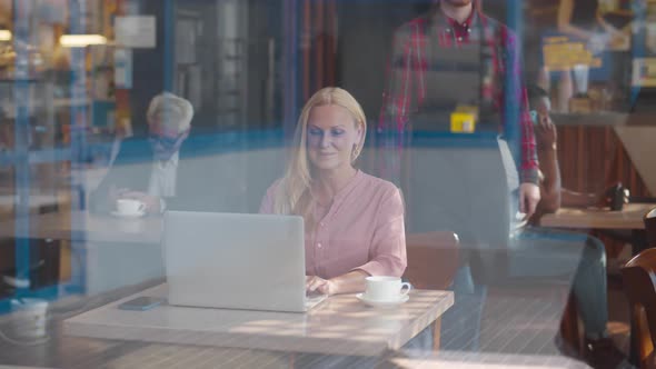 View Through Window of Mature Businesswoman Work on Laptop in Cafe