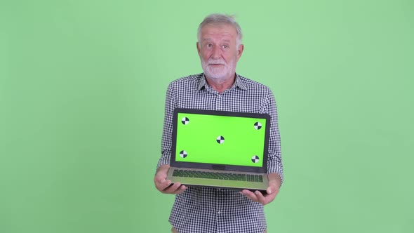 Happy Senior Bearded Man Talking While Showing Laptop