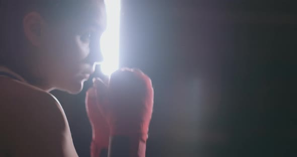 A Beautiful Woman Boxer Trains in a Dark Gym and Works Out Punches in Slow Motion. Side View