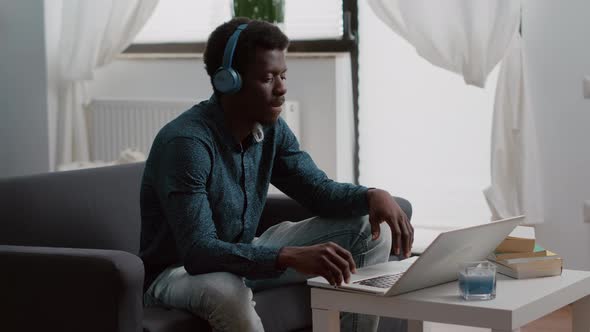 Authentic Smiling African American Man Using Laptop with Headphones on Working From Home