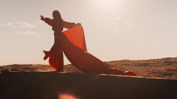 An Asian Woman in a Red Dress Dancing Against the Sun at Sunset on Sand Dunes
