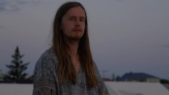 Young Man With Long Hair Meditating On City Roof