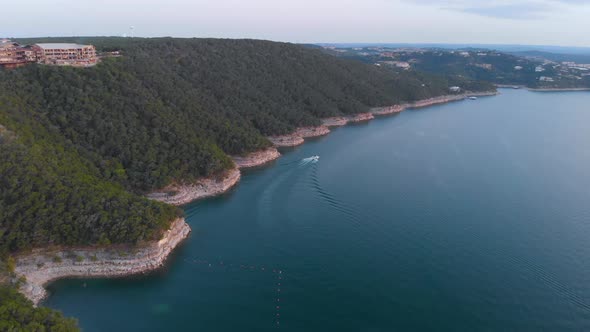 Very High Aerial shot of a boat following the cliffs along lake travis.