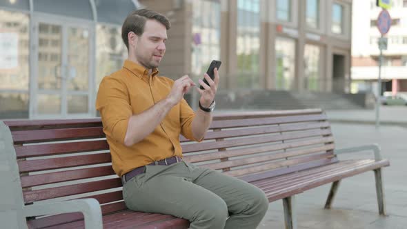 Young Man Celebrating Online Success on Smartphone Outdoor