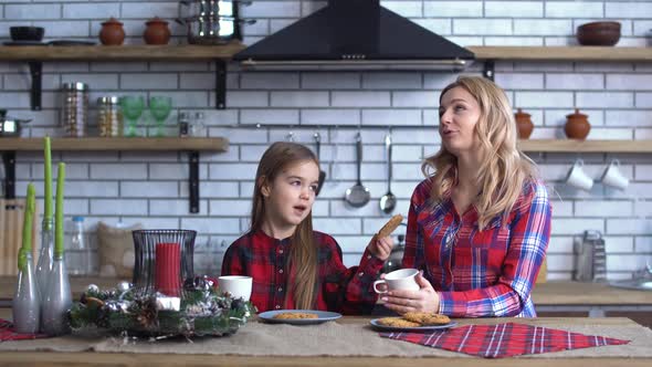 Mother with Long Blong Hair Sitting on Kitchen Table with Her Beautiful Daughter Which Feed Mom