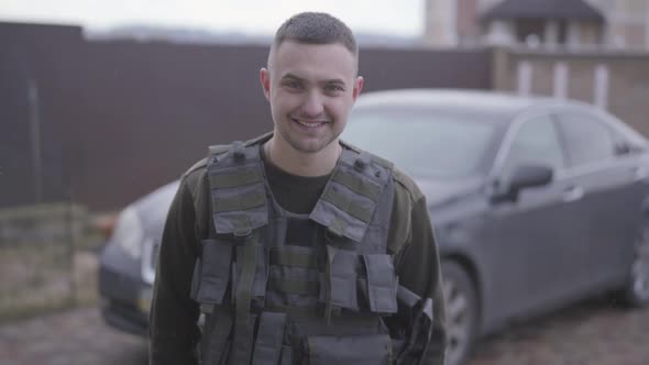 The Young Happy Man in Military Closes in the Bulletproof Vest Standing in Front of the Car