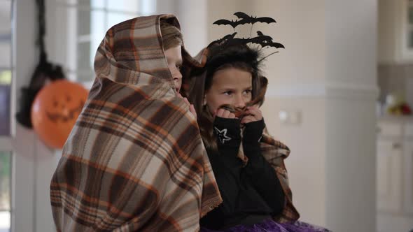 Scared Children Wrapped in Blanket Watching Horror Movie on Halloween Indoors