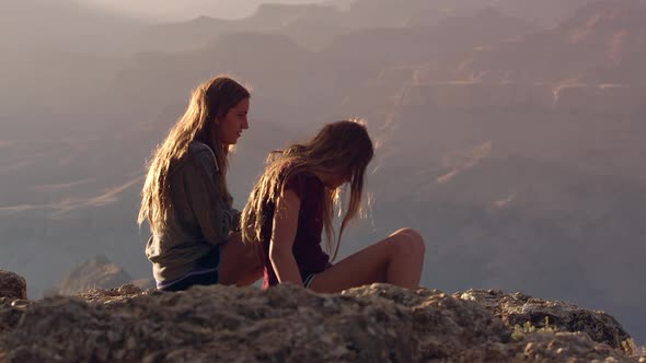 Teenage girls sitting on the edge of a cliff and tossing a rock