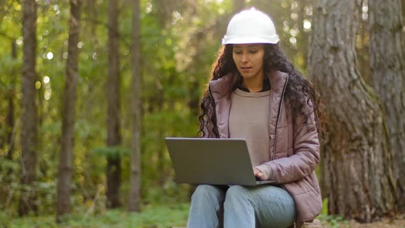 Attractive Woman Forestry Engineer in Protective Helmet Enters Data Into Laptop Takes Reforestation