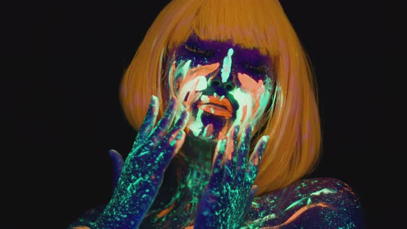 Young Carefree Woman with Art Neon Makeup and Orange Wig Dancing Smearing Fluorescent Paint on Her