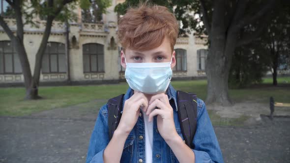 Little Redhead Boy Putting on Covid-19 Face Mask and Looking at Camera. Portrait of Caucasian