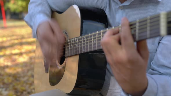 Men is Playing Black Acoustic Guitar Outside in the Yellow Autumn Park