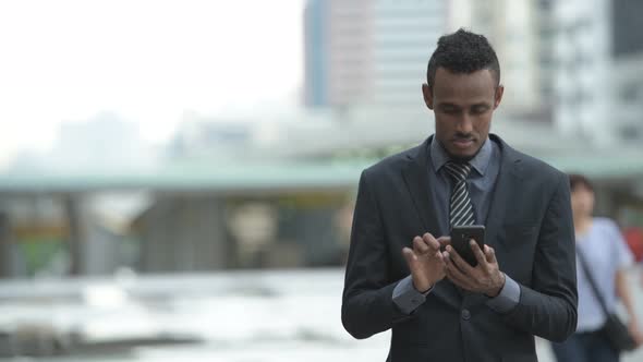 Happy Young African Businessman Thinking While Using Phone Outdoors