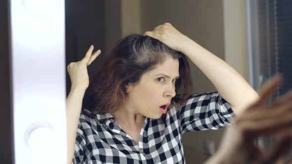 Young Frustrated Woman Looks in the Mirror and Plucks a Grey Hair From Her Head. Concept Photo of