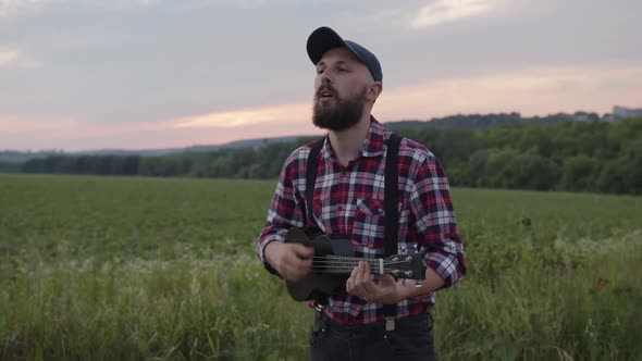 Attractive Bearded Young Man Plays on a Guitar