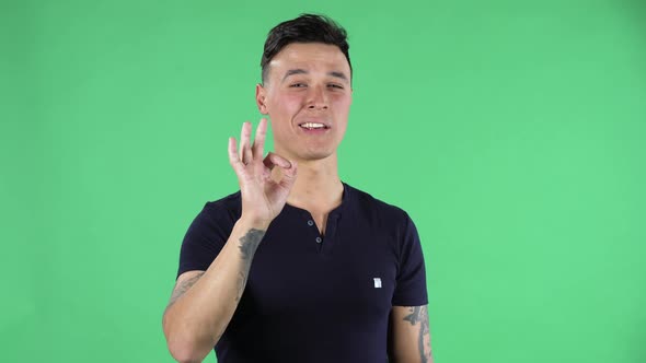 Portrait of a Handsome Young Guy Is Looking at the Camera and Making Sign Ok. Green Screen.