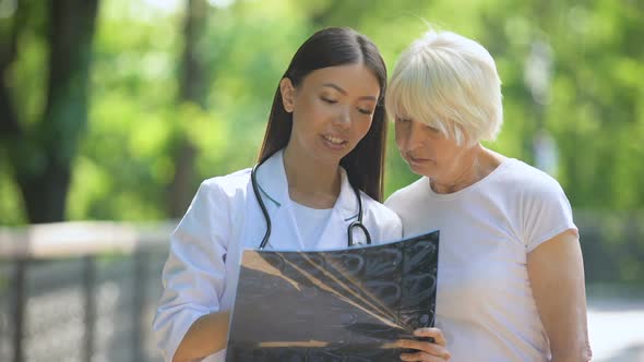 Nurse Showing Elderly Woman Joint X-Ray Examination Result, Smiling at Camera