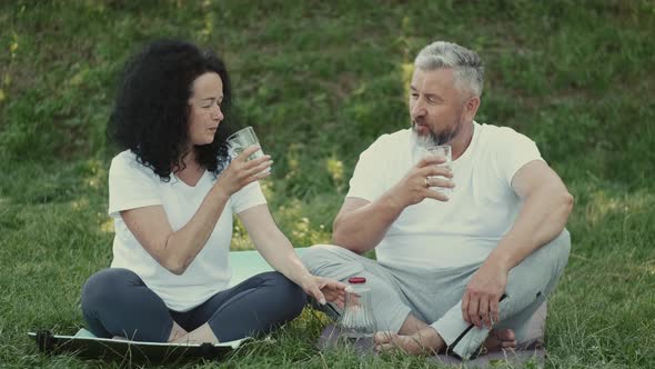 Man and Woman Are Drinking Water Sitting on the Lawn