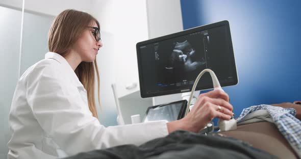 Focused Female Doctor Performs Ultrasound Examination of Internal Organs of Her