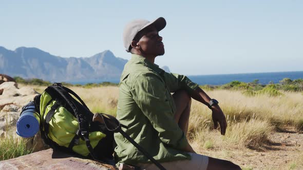 African american man hiking in countryside by the coast taking a rest sitting on a rock