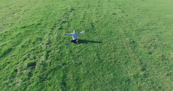 Low Orbital Flight Around Man on Green Grass with Notebook Pad at Yellow Rural Field