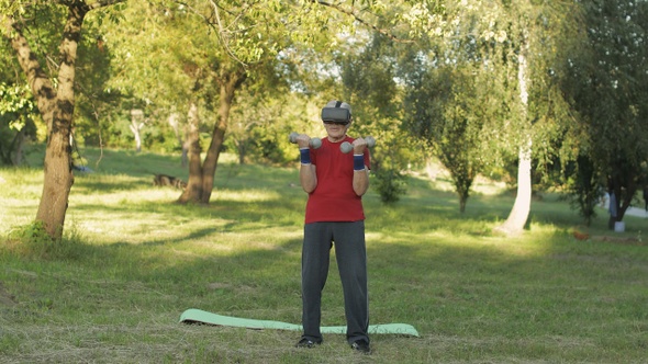 Senior Old Grandfather Man in VR Headset Helmet Making Fitness Exercises with Dumbbells in Park