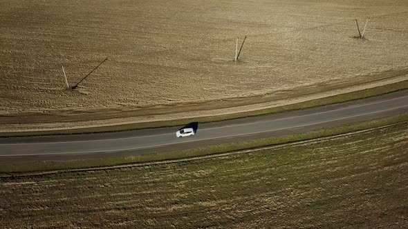 A White Car Is Driving Along an Asphalt Road Trip Among Fields. Aerial Shot Drone. Top View