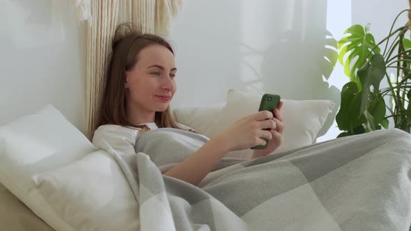 Smiling Woman Using a Mobile Phone Was Lying on the Bed