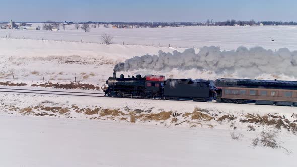 Aerial View of an Antique Steam Locomotive Approaching Pulling Passenger Cars and Blowing Smoke and Steam After a Snow Storm