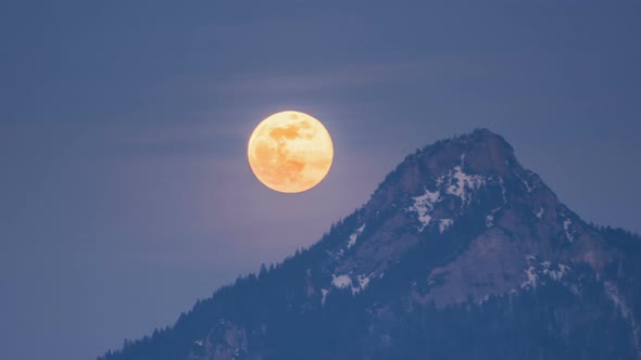 Big Golden Full Moon Rising over Alpine Mountains Peak in Winter Evening