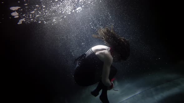 A Darkhaired Woman in Red Handcuffs is Swimming Deep Under the Water on a Dark Background