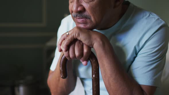 Senior mixed race man sitting thinking, leaning on walking stick