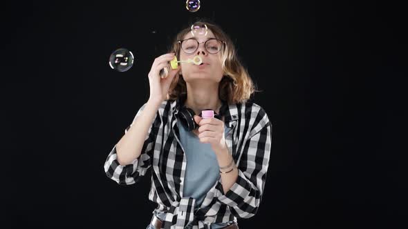 Portrait of Happy Girl in Glasses Blowing a Lot of Soap Bubbles with Stick on Black Background