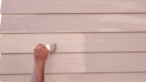 Builder worker painting woodwork brown color on cornice or moulding exterior outside home