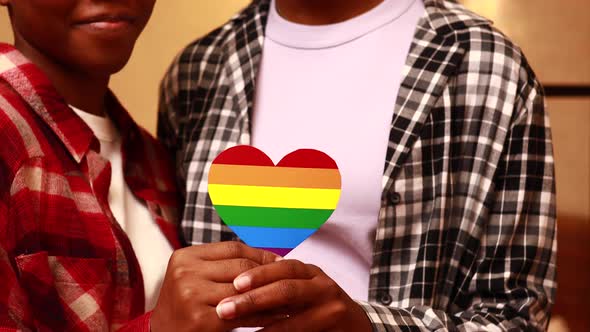 Two Mixed Race Women with Rainbow Heart Shape Cardboard in Home at Evening