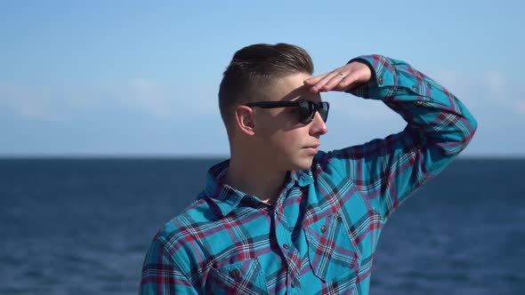 A Young Man on a Background of the Sea. Man in Sunglasses in Sunny Weather. Explores the Nature