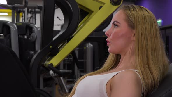 A Young Beautiful Woman Trains on a Leg Press Machine in a Gym - Closeup From the Side