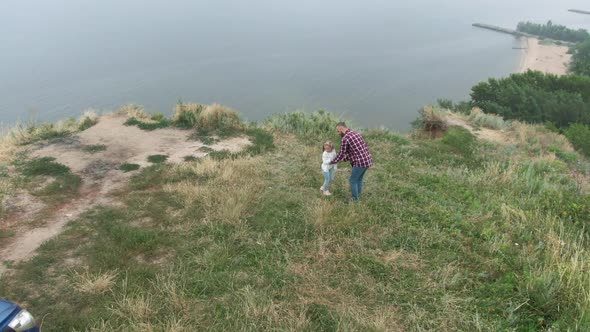 Drone View of Father Spinning Little Daughter on Cliff Over River Having Fun Enjoying Leisure