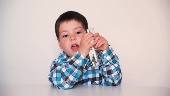 A Preschool Boy Drinks Water From a Glass Smiles and Talks Looking Into the Camera