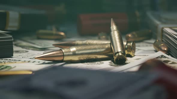 Few ammo bullets on a table in the dark covered with countless dollar bills.4KHD