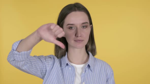 Young Woman Gesturing Thumbs Down on Yellow Background