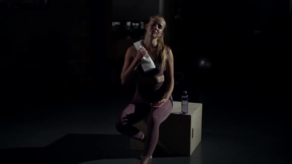 Wide Shot Charming Smiling Woman Hanging Towel on Shoulder in Slow Motion Sitting on Cube in Gym
