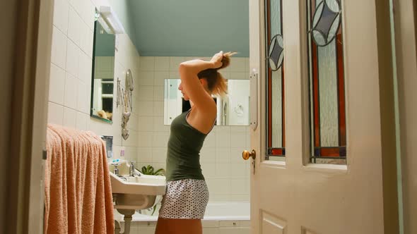 Woman tying her hair in bathroom at home 4k
