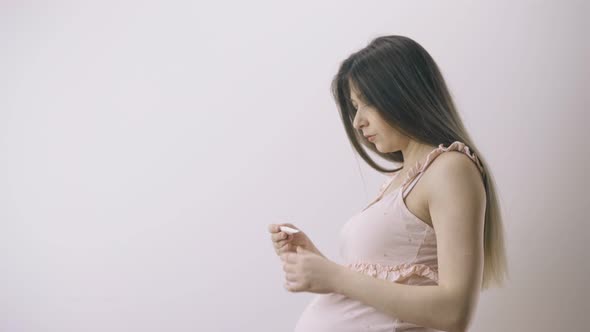 Pregnant Woman in Pink Dress Measures Temperature in Room