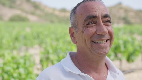 Happy Caucasian Male Winemaker Smiling Looking Away with Blurred Plantation at Background